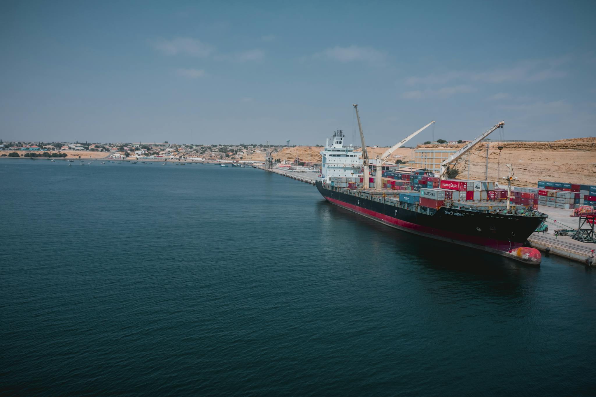 Cargo ship docked at Namibe port in Angola with shipping containers and cranes.